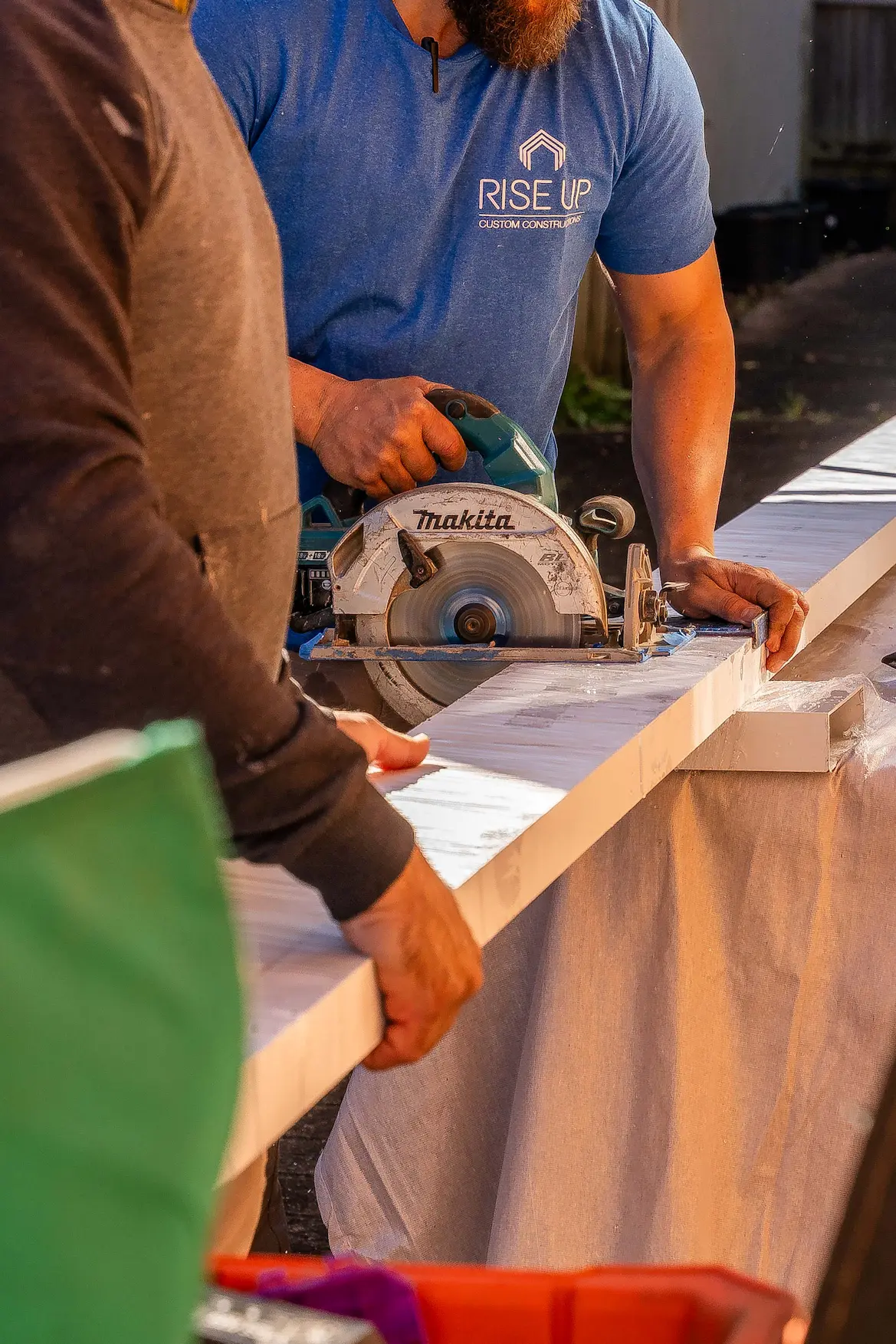 Rise Up crew cutting a powder-coated aluminium section with a circular saw during the Killara carport build